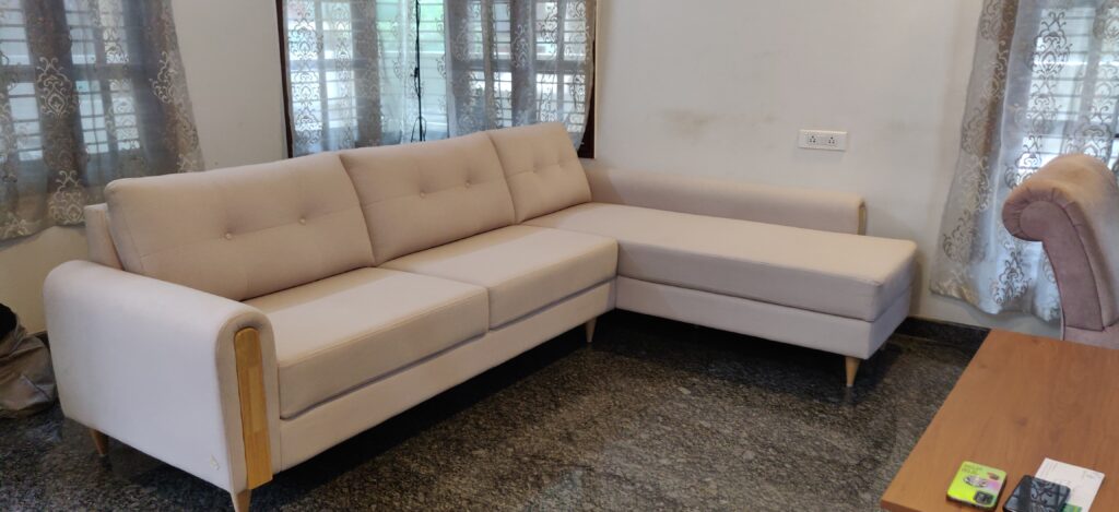 Beige fabric L-shaped sofa with wooden arm accents in a living room