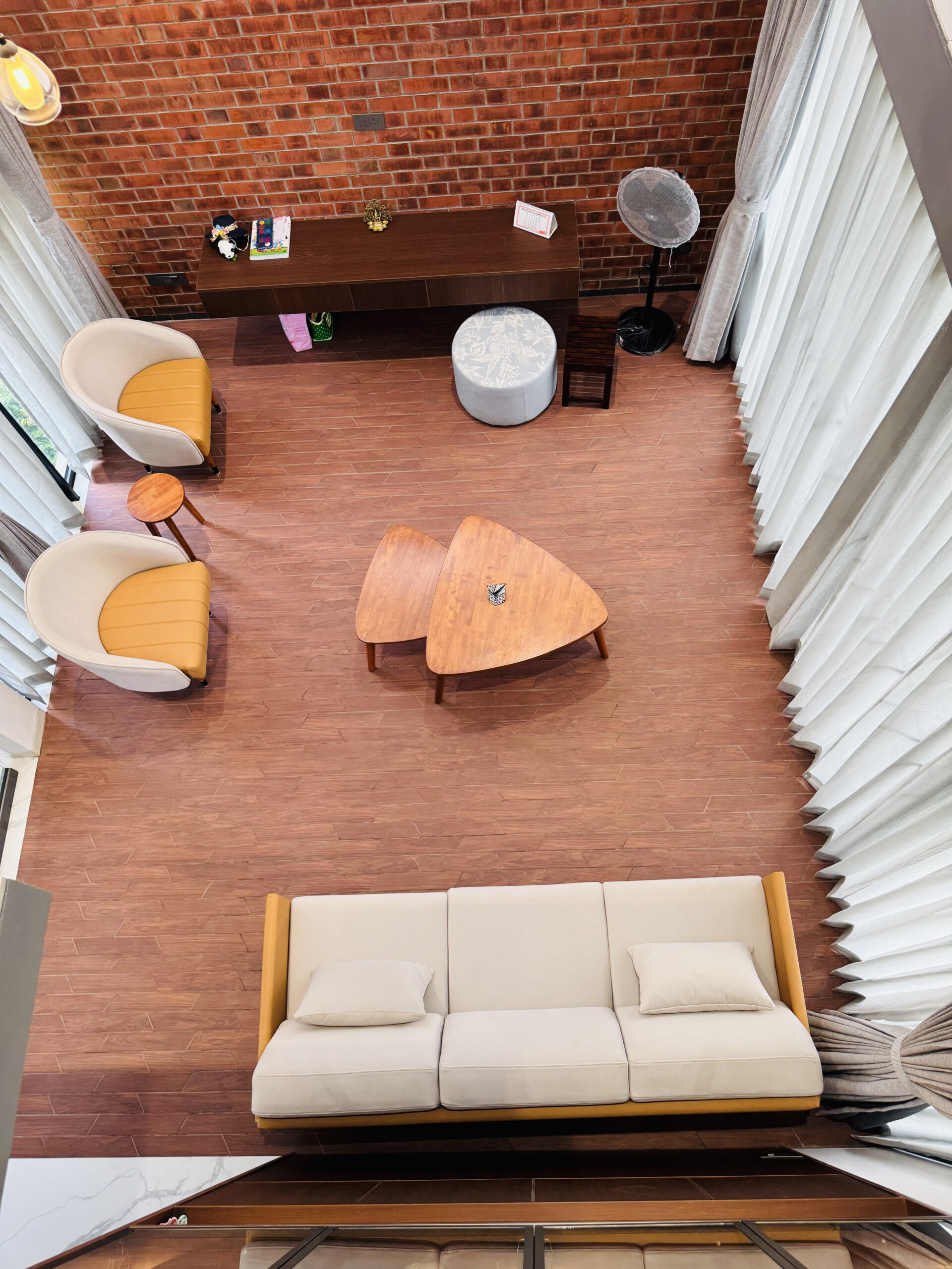 Living room seen from above with a cream sofa, wooden coffee tables and lounge chairs