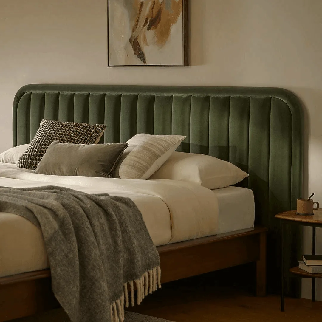 Wooden cot with a green channel-tufted upholstered headboard and layered bedding