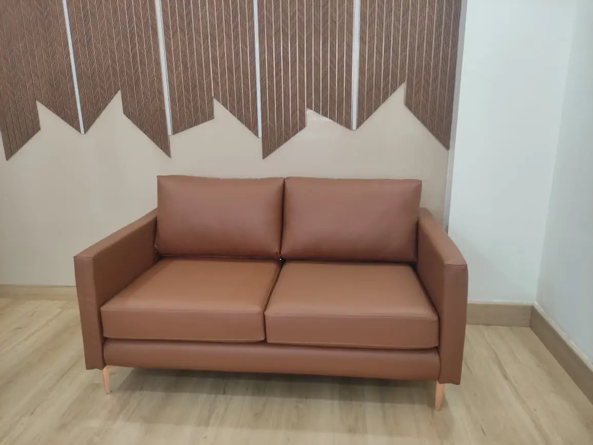 Brown leatherette 2 seater sofa with slim arms and wooden legs against a textured feature wall