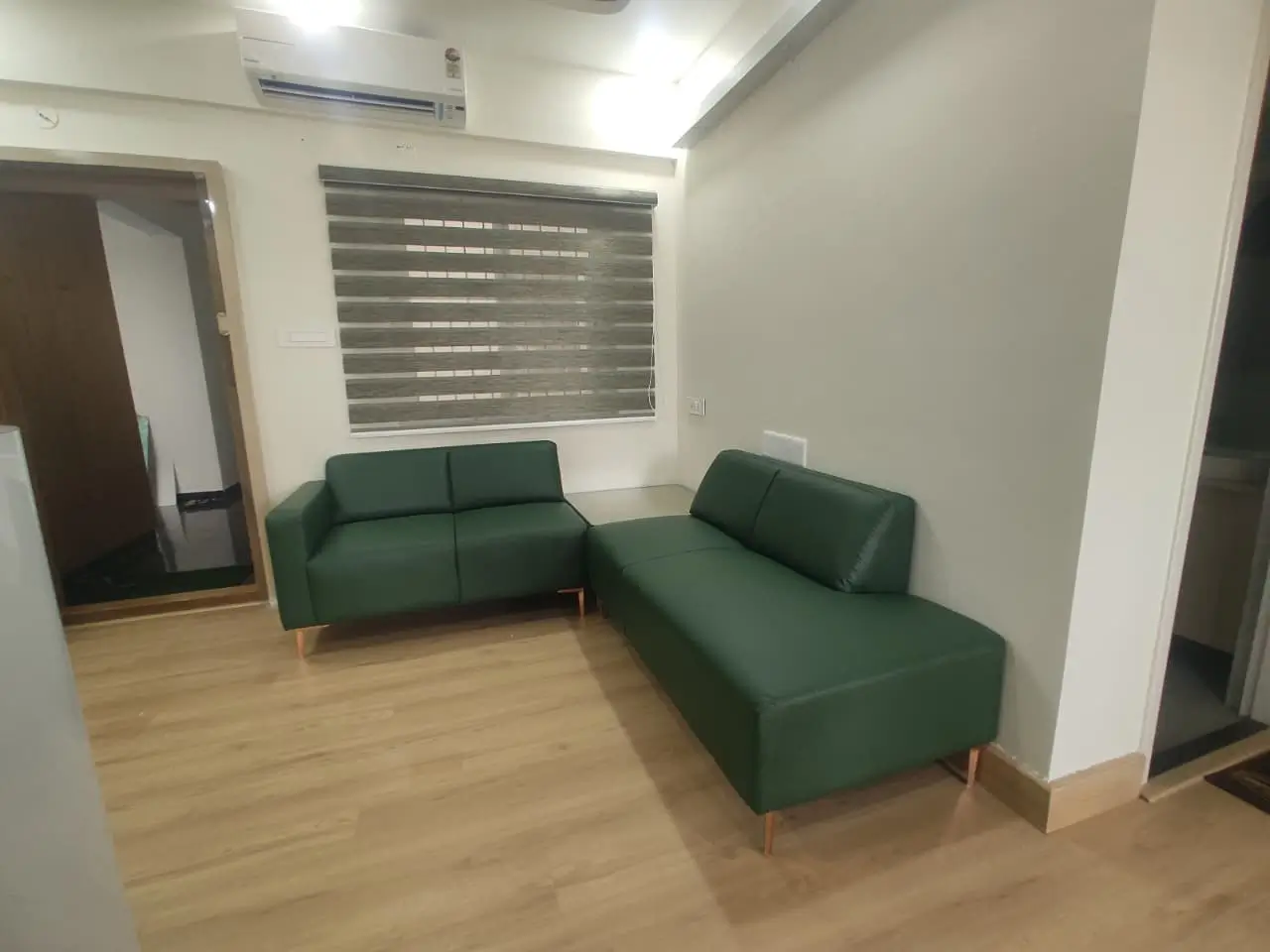 Green leatherette L-shaped corner sofa with wooden legs in a compact living room