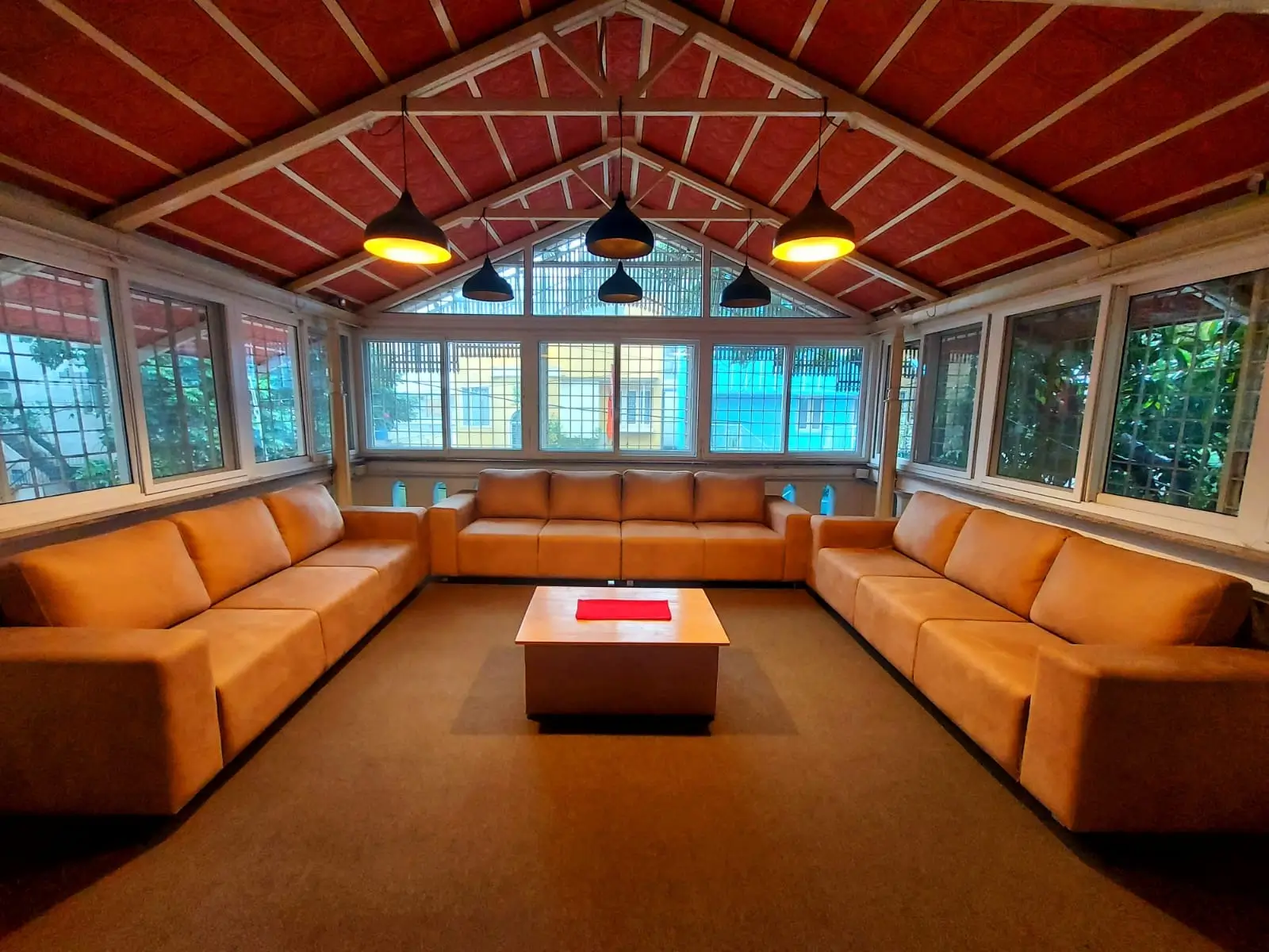 Orange U-shaped 10 seater sofa set arranged around a coffee table in a large sunroom with wooden roof beams